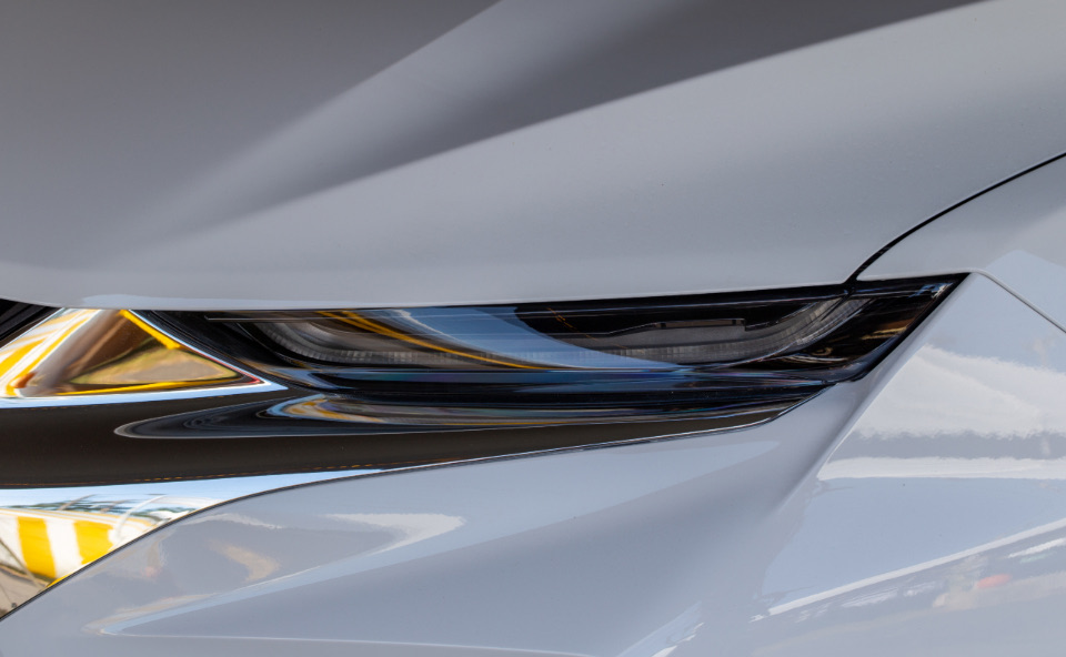 Front corner of a silver car with a minor low-speed dent near the headlight