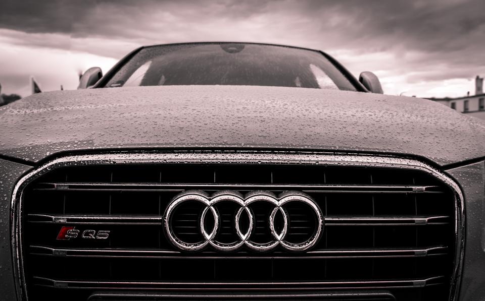 Hood of a dark car under a storm sky, the kind of panel hail dents