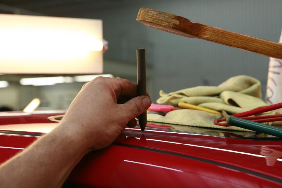 A technician working a dent out of a car panel by hand